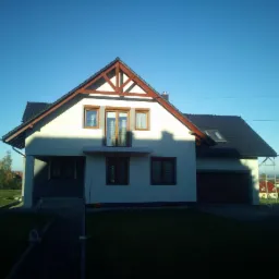 Nowoczesny dom jednorodzinny z jasną elewacją, ciemną dachówką i drewnianymi elementami dekoracyjnymi pod dachem, sfotografowany w słoneczny dzień z widokiem na zadbany trawnik i okoliczne...