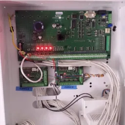 Otwarta skrzynka z elektroniką alarmową Safetel Integra 128, widoczne diody sygnalizacyjne, liczne przewody oraz moduły oznaczone 'Adres 8' i 'Adres 9'.