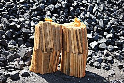 Dwie siatki z ułożonym drewnem kominkowym na tle węgla kamiennego, oświetlone jasnym światłem słonecznym.