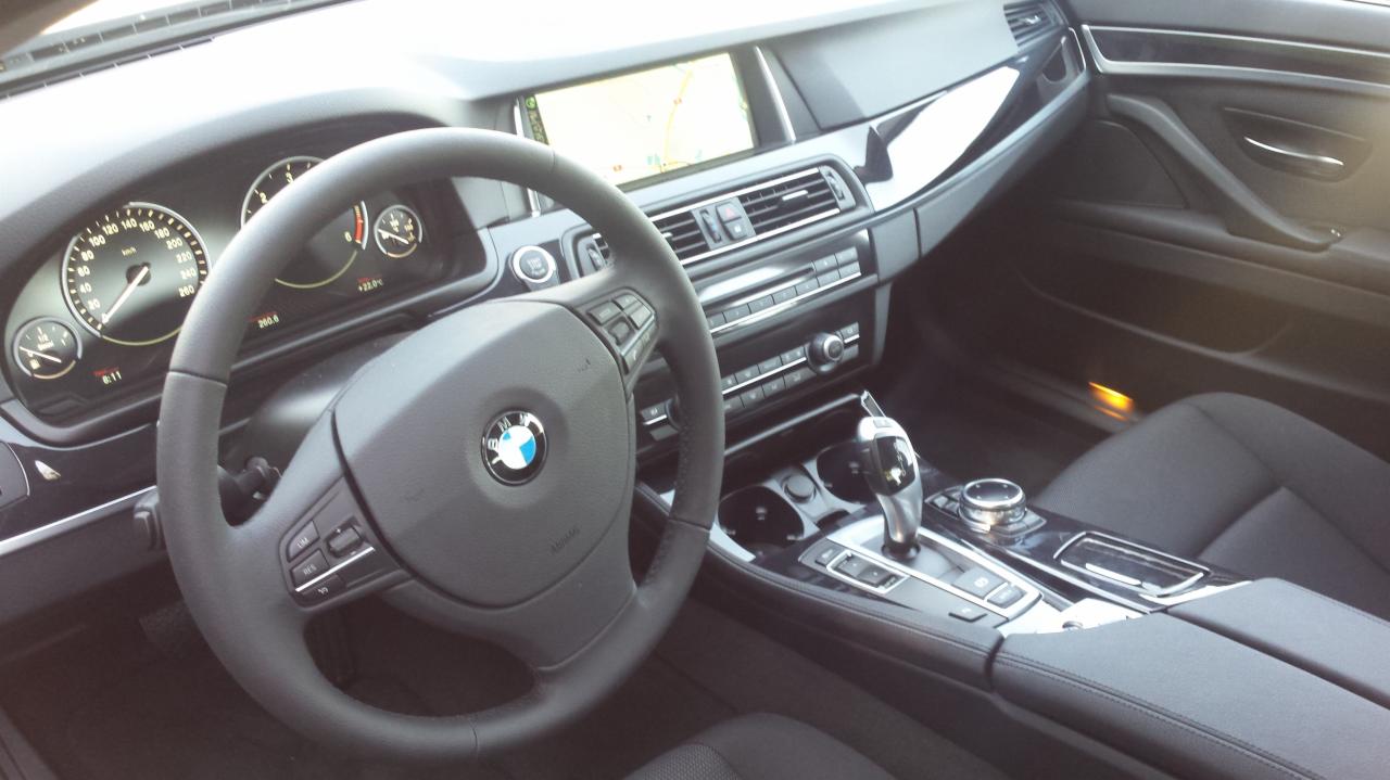 Wnętrze czarnego BMW serii 5 z widoczną deską rozdzielczą, kierownicą z logo BMW oraz nawigacją. Nowoczesny design i eleganckie wykończenie.