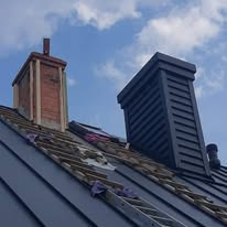 Nowe, grafitowe pokrycie dachowe z dwoma kominami: starym ceglanym i nowym, obłożonym szarymi panelami. Widoczne elementy konstrukcji dachu i drabina oparta o dach.