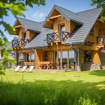 Nowoczesny dom z bali z ciemnoszarym dachem dwuspadowym, widoczne balkony z czarnymi balustradami, jasne drewniane wykończenie, zadbany trawnik na pierwszym planie.