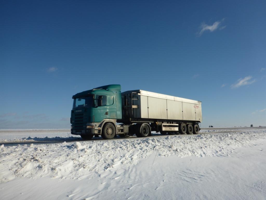 Ciężarówka Scania z naczepą na ośnieżonej drodze, błękitne niebo w tle.
