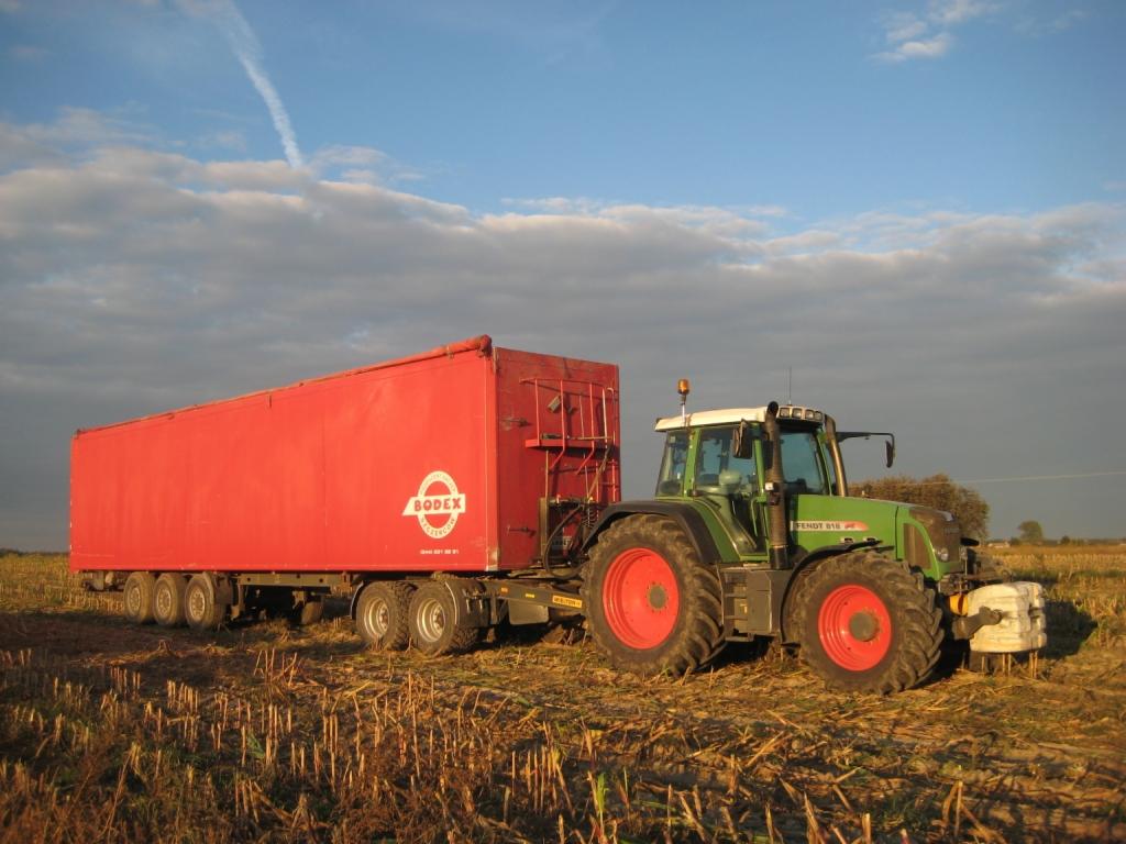 Zielony traktor Fendt 916 z czerwoną przyczepą Bodex na polu po żniwach, widoczne ślady opon i chmury na niebie.