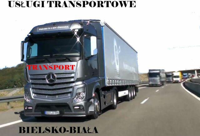 Szary ciągnik siodłowy Mercedes-Benz z naczepą na autostradzie, napis TRANSPORT na kabinie, w tle inne ciężarówki i tablica z napisem BIELSKO-BIAŁA.