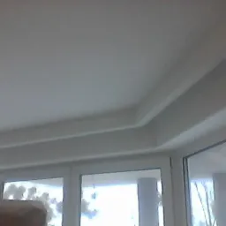 Biały sufit z dekoracyjnym gzymsem przy oknach w pokoju, widok z dołu.