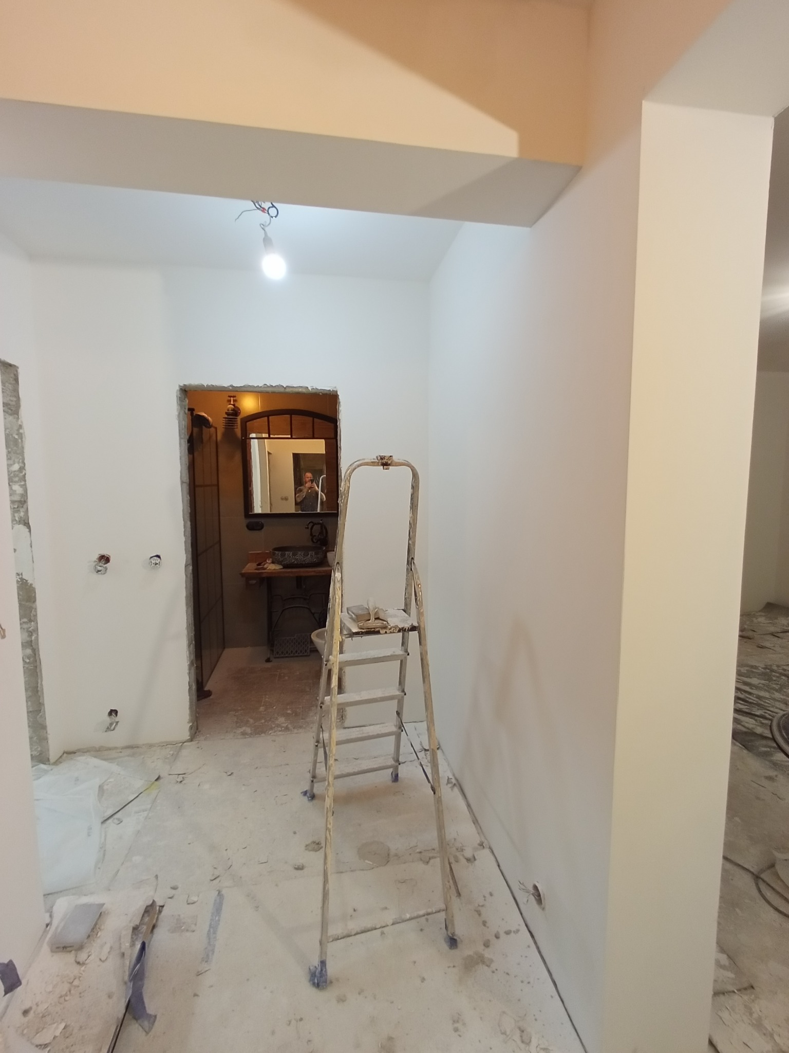 Wnętrze w trakcie prac, widoczna drabina malarska, świeżo pomalowane ściany na biało, przygotowane do dalszych prac wykończeniowych, zarys łazienki w tle.