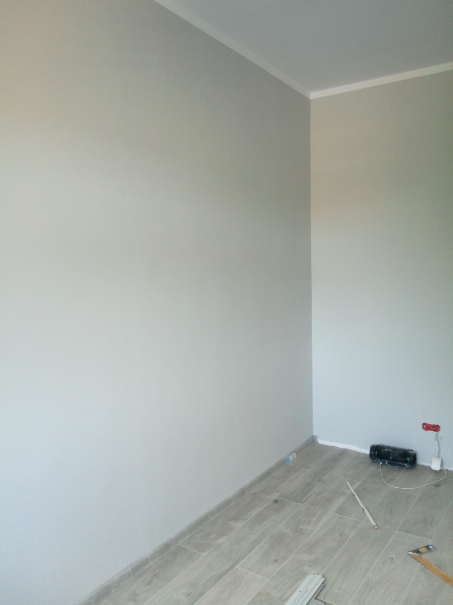 Pomalowane na szaro wnętrze pokoju z ułożoną podłogą z paneli imitujących drewno, widoczne listwy przypodłogowe, gniazdka elektryczne i narzędzia.