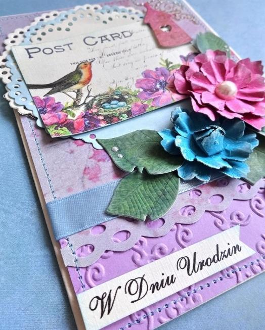 Ręcznie robiona kartka urodzinowa z motywem ptaka, kwiatów i napisem 'W Dniu Urodzin' na fioletowym tle z wytłaczanym wzorem i dekoracyjną wstążką.