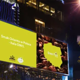 Billboard reklamowy nocą z hasłem 'Smak Orientu w Polsce - hala OW1' i grafiką w kształcie Polski wypełnionej logiem Green Palm na tle daktyli.