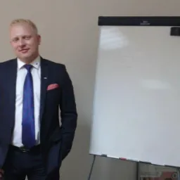 Doradca finansowy w garniturze pozuje obok flipcharta z notatkami, prezentując profesjonalizm i gotowość do omówienia strategii finansowych.