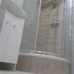 Nowoczesna łazienka z kabiną prysznicową typu walk-in, umywalką z szafką i płytkami imitującymi drewno na ścianach.