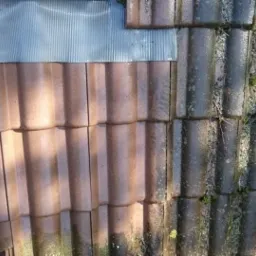 Częściowo wyczyszczony dach z brązowej dachówki ceramicznej, widoczna różnica między umytą a zabrudzoną powierzchnią, z mchem i zanieczyszczeniami.