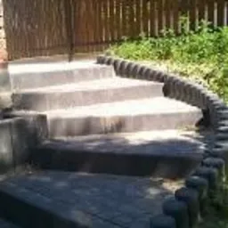 Schody z kostki brukowej prowadzące pod górę, otoczone drewnianym płotem w tle, ujęcie z dołu, w słoneczny dzień.