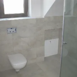 Wykończona łazienka z podwieszaną toaletą, jasnymi płytkami imitującymi kamień i zabudowanym stelażem podtynkowym z dostępem serwisowym.