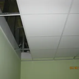 Montaż sufitu podwieszanego kasetonowego z odsłoniętą konstrukcją i widoczną izolacją poddasza, ściana w kolorze pistacjowym.