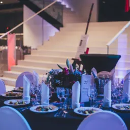 Uroczysta dekoracja stołu z kwiatami, zastawą i menu numer 27, ustawiona w sali z białymi schodami i oświetleniem punktowym.