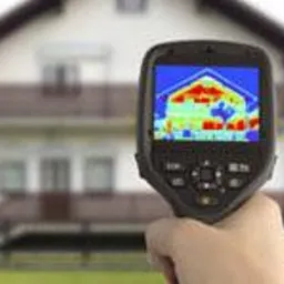 Termowizja domu jednorodzinnego. Kamera termowizyjna w dłoni, na ekranie rozkład temperatur budynku. Analiza strat ciepła i efektywności energetycznej.