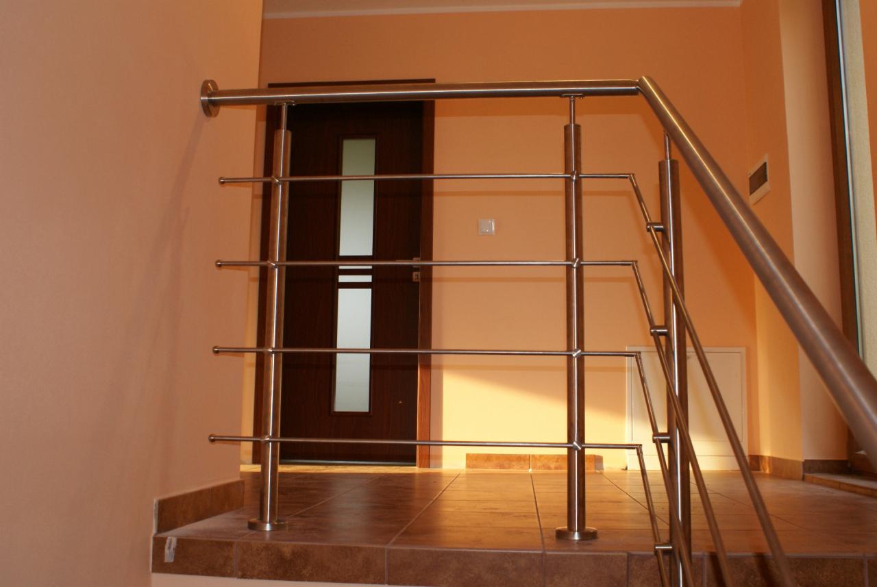 Nowoczesna, metalowa balustrada schodowa ze stali nierdzewnej z poziomymi prętami, na tle brązowych płytek podłogowych i drzwi z przeszkleniem.
