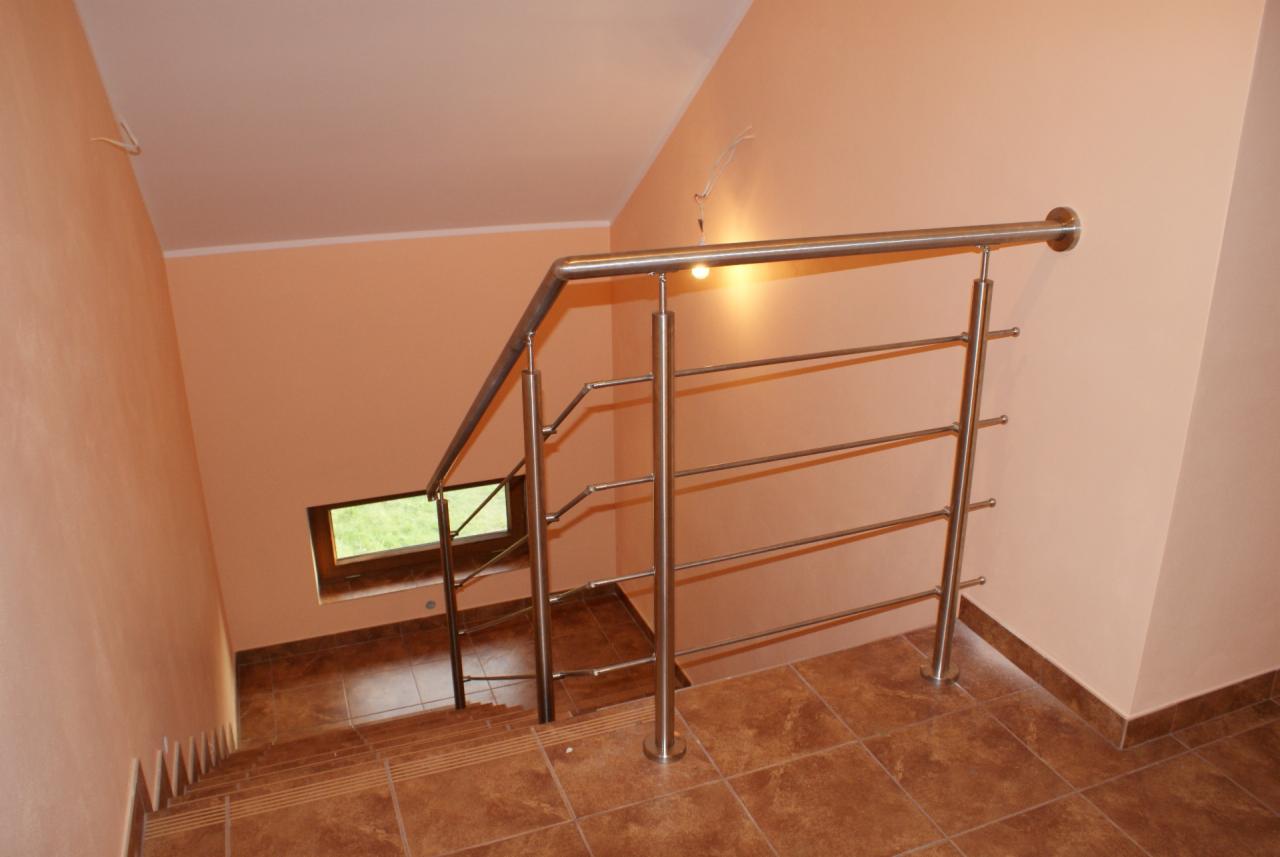 Wewnętrzne schody z brązowych płytek z metalową, nowoczesną balustradą ze stali nierdzewnej. W tle małe okno.