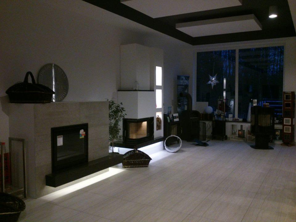 Salon z dwoma kominkami o różnych stylach: nowoczesny biały i klasyczny z okładziną. Duże okno z widokiem na nocny krajobraz. Dekoracje na kominkach.