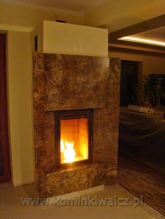 Kamienny kominek z paleniskiem, płomienie widoczne przez szybę, ciepłe światło w pomieszczeniu. Dekoracyjny element wykończenia wnętrza.