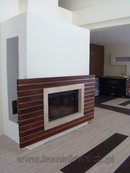 Nowoczesny kominek z obudową z poziomych, ciemnych desek i jasnym obramowaniem paleniska, w jasnym wnętrzu z wzorzystą podłogą. Minimalistyczny design.