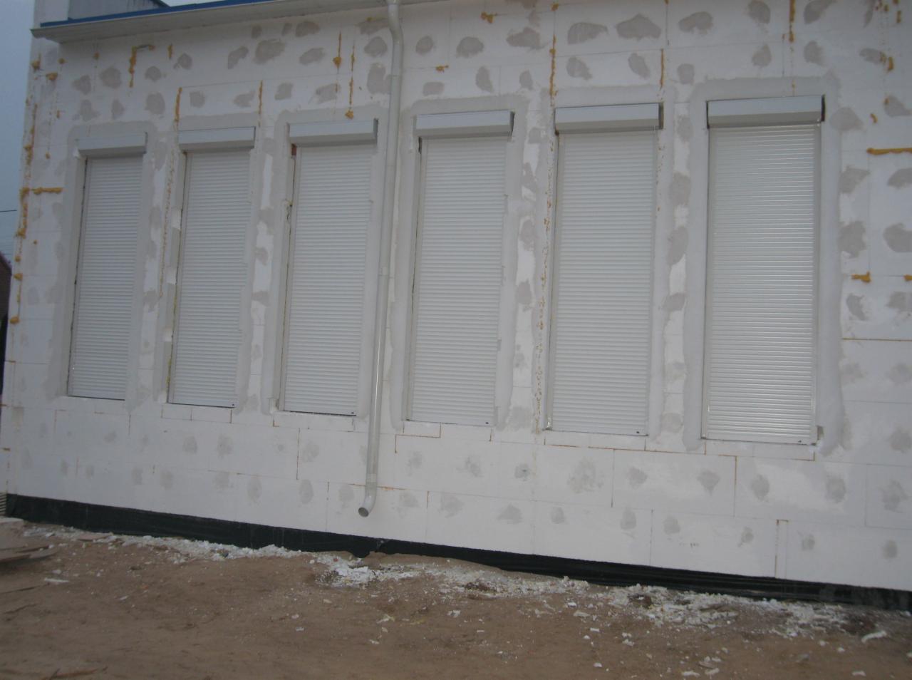 Montaż rolet zewnętrznych na oknach w trakcie ocieplania elewacji budynku, widoczne niedoskonałości i ślady po kleju na styropianie.