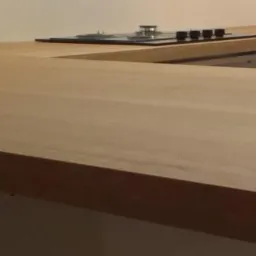 Beżowy, drewniany blat kuchenny w kształcie litery U, z widoczną płytą grzewczą, zamontowany na białych szafkach. Widok z bliska na strukturę drewna.