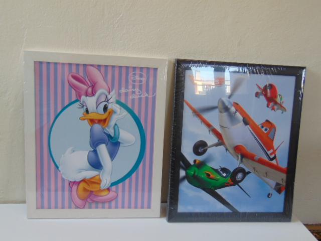 Dwa oprawione plakaty: Daisy Duck w różowo-białej ramce i samoloty z filmu 'Planes' w czarnej ramce, stojące obok siebie na białym tle.