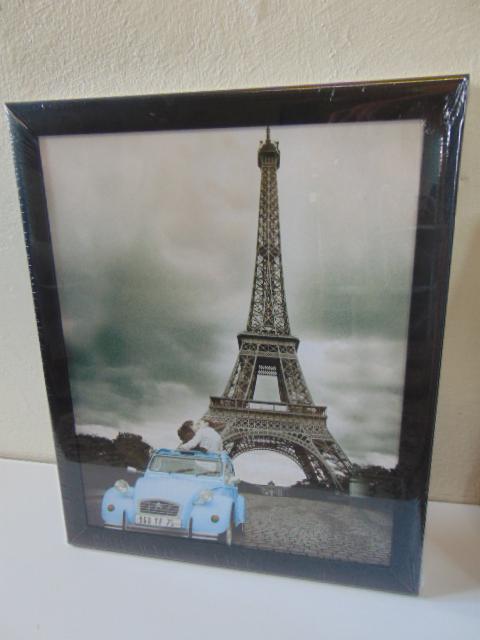 Oprawiony plakat z wieżą Eiffla, parą w niebieskim samochodzie. Czarna rama, błyszcząca folia ochronna. Romantyczny motyw, dekoracja wnętrz.
