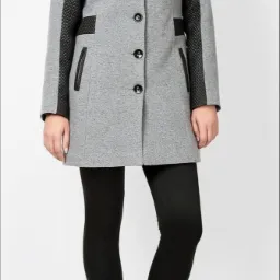 Szary płaszcz damski z czarnymi, pikowanymi wstawkami na ramionach i kołnierzu, zapinany na trzy guziki, noszony z czarnymi legginsami i sznurowanymi botkami.