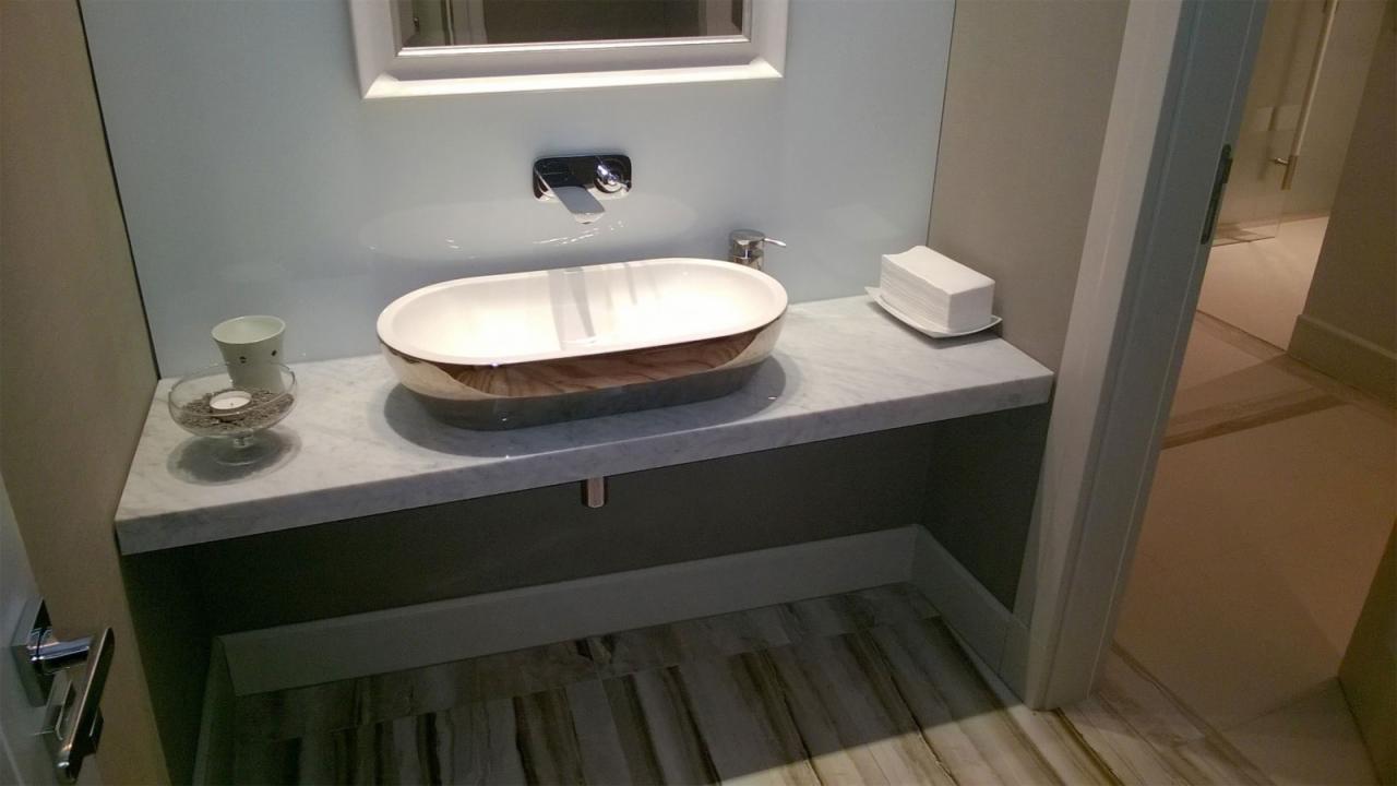 Elegancka łazienka z owalną umywalką z drewnianym akcentem na marmurowym blacie. Minimalistyczna armatura i podłoga w odcieniach brązu.