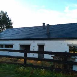 Surowy stan domu jednorodzinnego w Chocianowie, z ciemną dachówką i widocznymi kominami, ogrodzony prowizorycznym drewnianym płotem, w tle drzewa.