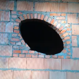 Murowanie owalnego okna z cegły klinkierowej w ścianie z bloczków, widoczne ślady zaprawy, budowa w Połajewie. Nietypowy kształt okna.