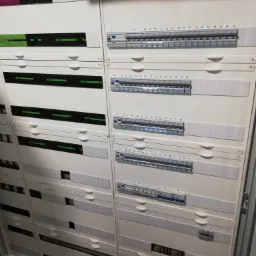 Rozdzielnica elektryczna z numerowanymi bezpiecznikami i modułami, widoczne okablowanie i oznaczenia.