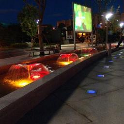 ARTMARE Sp. z o.o. - Nocne ujęcie fontanny z kolorowym podświetleniem i wbudowanymi lampami w chodniku, tworzącymi efektowny wizualny krajobraz miejski.