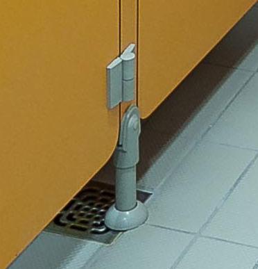 Szczegół mocowania żółtej ścianki działowej do podłogi z szarych płytek, widoczny zawias z tworzywa sztucznego oraz metalowa kratka odpływowa w podłodze.