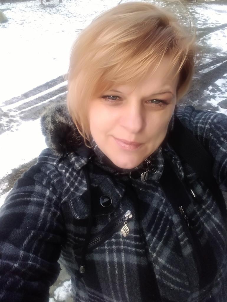 Portret kobiety w zimowej kurtce w kratę z ozdobnymi zawieszkami przy zamkach, na tle śniegu.