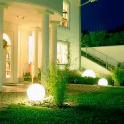 Oświetlone kule dekoracyjne w ogrodzie przed domem z kolumnami, widoczne schody na zewnątrz budynku.