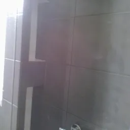 Szare płytki w łazience z wnęką i chromowaną armaturą. Nowoczesne wykończenie ściany w kabinie prysznicowej, widoczny fragment baterii.