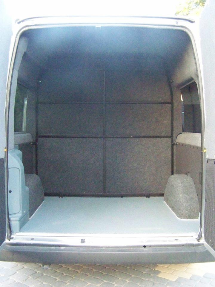 Wykończone wnętrze furgonetki z panelami ściennymi i podłogą, przygotowane do transportu. Widok z otwartych tylnych drzwi.