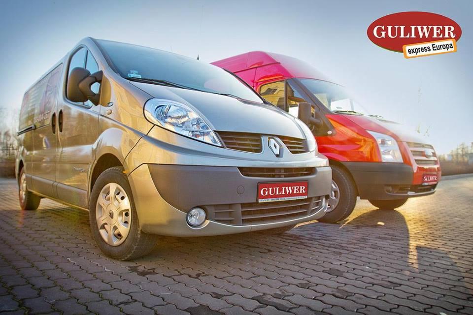 Dwa busy transportowe: srebrny Renault i czerwony Ford, zaparkowane na brukowanej nawierzchni. Widoczne logo firmy 'Guliwer express Europa'.