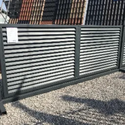 Nowoczesna, przesuwna brama wjazdowa z poziomymi panelami w odcieniach szarości, prezentowana na żwirowym podłożu, z widoczną kartką informacyjną na jednym z paneli.