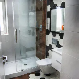 Wnętrze małej łazienki z kabiną prysznicową ze szklanymi drzwiami przesuwnymi, toaletą podwieszaną i umywalką, wykończonej płytkami heksagonalnymi w kolorze czarnym i białym oraz panelami...