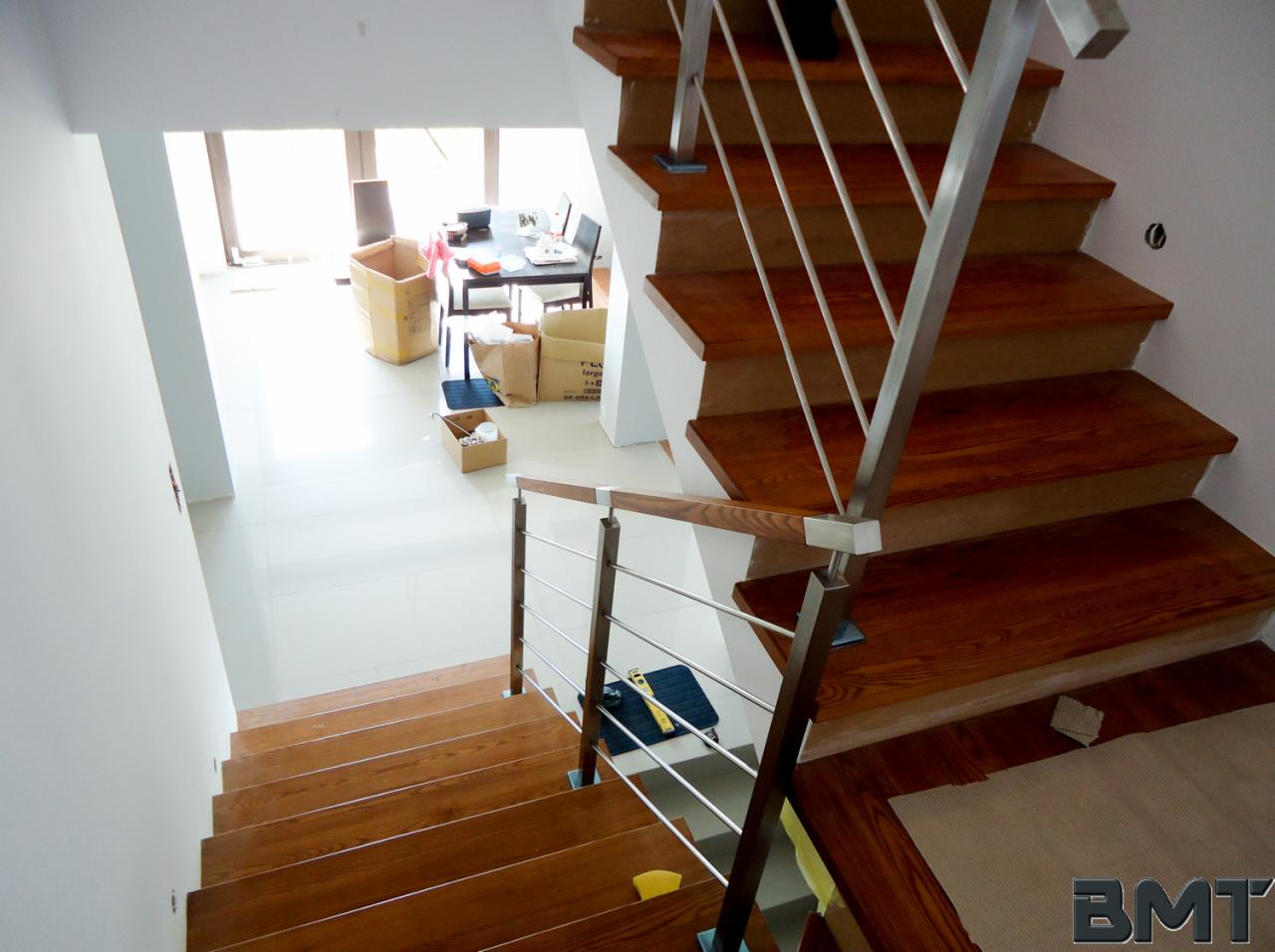 Drewniane schody z metalową balustradą, widok z góry. Jasne wnętrze, w tle kartony. Elementy montażowe na stopniach. Nowoczesny design.