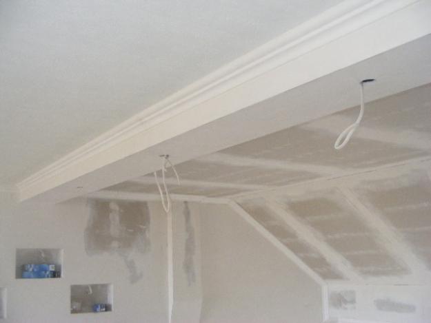 Wykończenie sufitu z listwą dekoracyjną i wystającymi przewodami elektrycznymi. Ściany przygotowane pod malowanie, widoczne wnęki ścienne.