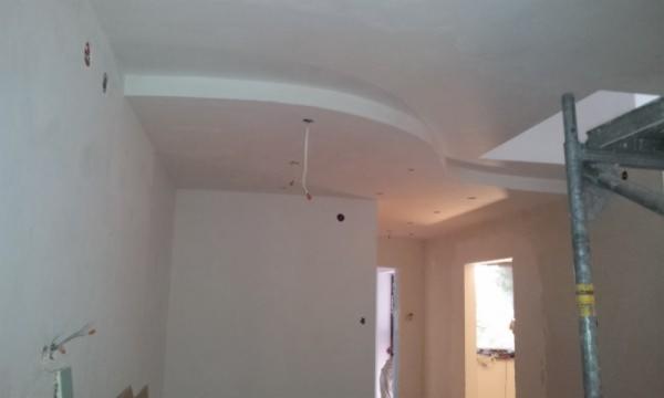 Wykończone, gładkie ściany i sufit z dekoracyjnym, łukowym elementem. Widoczne przygotowania do instalacji oświetlenia i fragment rusztowania.