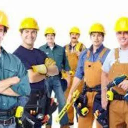 Grupa uśmiechniętych robotników budowlanych w kaskach i kombinezonach, z narzędziami, na białym tle. Jeden z nich trzyma wiertarkę.