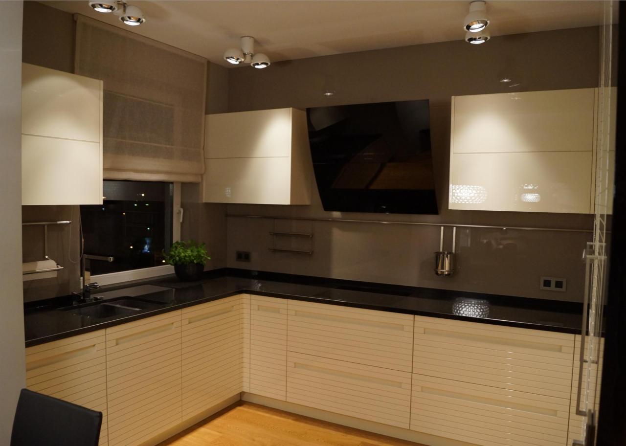 Nowoczesna kuchnia z beżowymi szafkami z poziomymi żłobieniami, czarnym blatem, czarnym okapem i punktowym oświetleniem sufitowym.